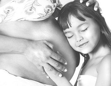 dziewczynka przytulona do ciążowego brzucha kobiety